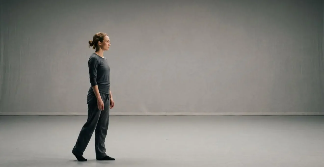 Environmental wide shot showing performer's body responding in sequence to off-stage stimulus with intentional negative space