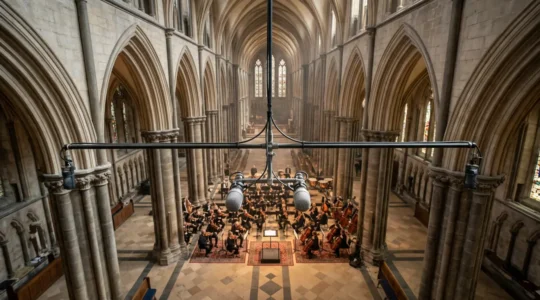 High-ceiling cathedral interior with omnidirectional microphones suspended above conductor podium capturing classical orchestra performance in natural reverberant space