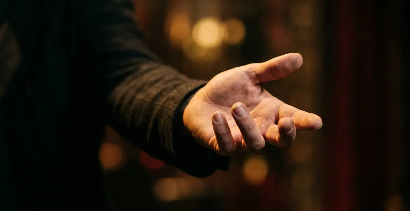 Close-up of a performer's outstretched hand reaching toward an unseen audience member in soft theatrical lighting