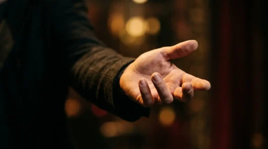 Close-up of a performer's outstretched hand reaching toward an unseen audience member in soft theatrical lighting