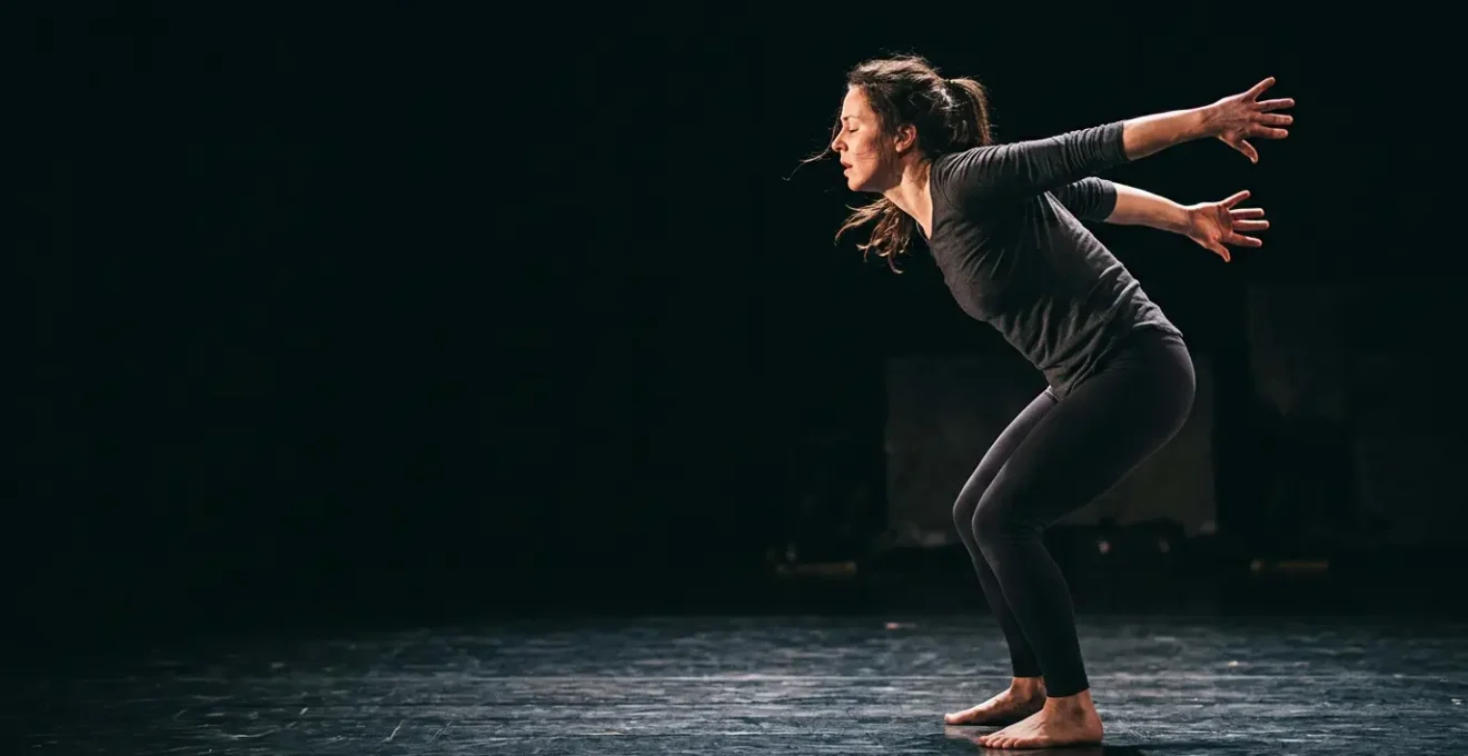 A physical theatre performer in mid-movement conveying intense emotion through body language alone