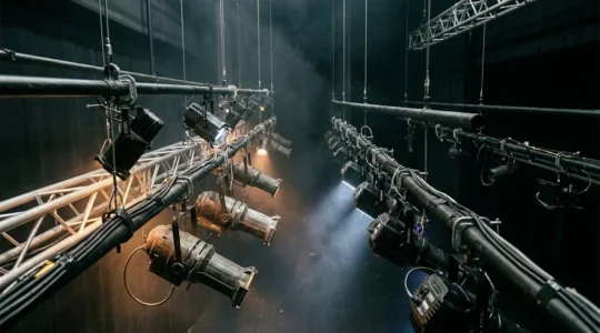 Professional theatre stage lighting system showing modern LED fixtures and traditional tungsten equipment in architectural rigging context